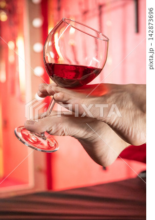 Foot fetish. A woman holds a glass of red wine with her feet. 142873696