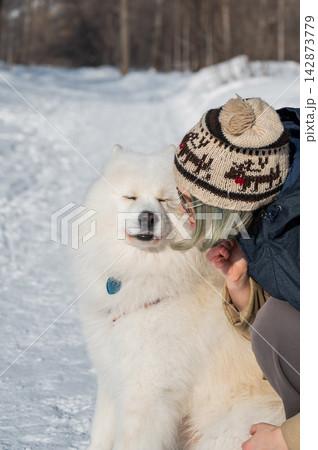 Young woman walking with fluffy samoyed dog in snowy winter park.  142873779