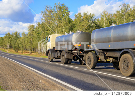 Silver Milk Tanker Truck Moving Along Countryside Road. Agriculture Liquid Cargo Logistics Silver Milk Tanker Truck Moving Along Countryside Road. Agriculture Liquid Cargo Logistics 142873809