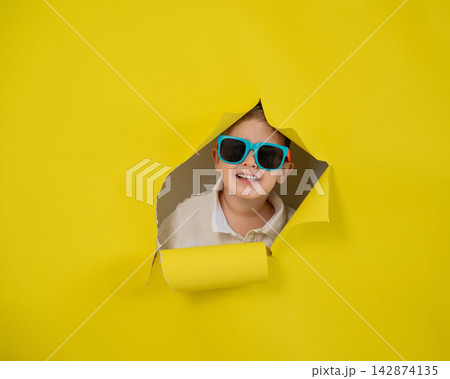Caucasian little boy in sunglasses tearing yellow paper background. Caucasian little boy in sunglasses tearing yellow paper background. 142874135