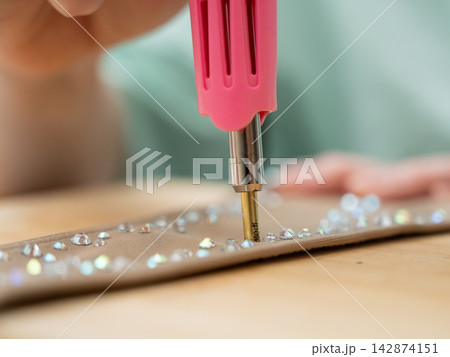 A woman glues rhinestones onto a gymnastics costume using a soldering iron. Hot fix. A woman glues rhinestones onto a gymnastics costume using a soldering iron. Hot fix. 142874151