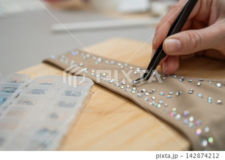 A woman decorates a gymnastics costume with rhinestones. Rhythmic gymnastics. Arranging with tweezers. A woman decorates a gymnastics costume with rhinestones. Rhythmic gymnastics. Arranging with tweezers. 142874212