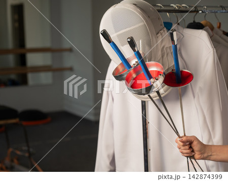 Fencing uniforms and masks hang on hangers. No people.  142874399