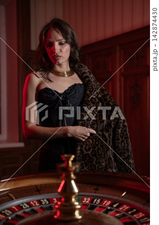 A beautiful brunette in a black dress at the casino roulette wheel. A beautiful brunette in a black dress at the casino roulette wheel. 142874430