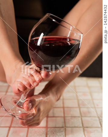Foot fetish. A woman pours wine from a glass onto her feet in the shower. Foot fetish. A woman pours wine from a glass onto her feet in the shower. 142874432