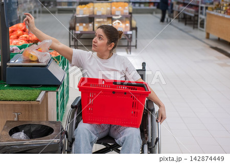 A Caucasian woman in a wheelchair buys fruit at a supermarket. A Caucasian woman in a wheelchair buys fruit at a supermarket. 142874449