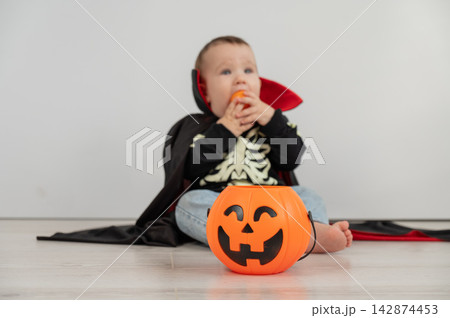 Cute caucasian boy in dracula halloween costume holding candy basket on white background.  142874453