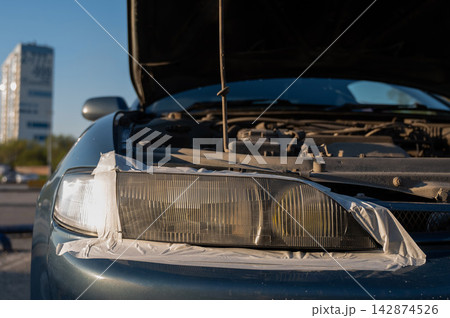 Close-up of a car headlight covered with tape around the perimeter during polishing. Close-up of a car headlight covered with tape around the perimeter during polishing. 142874526