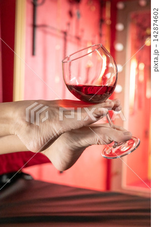 Foot fetish. A woman holds a glass of red wine with her feet. Foot fetish. A woman holds a glass of red wine with her feet. 142874602