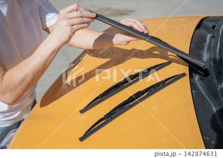 A woman replaces old windshield wipers with new ones on a car. A woman replaces old windshield wipers with new ones on a car. 142874631