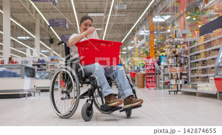 A Caucasian woman in a wheelchair buys fruit at a supermarket. A Caucasian woman in a wheelchair buys fruit at a supermarket. 142874655