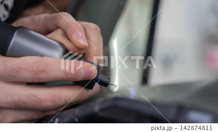 A technician drills a hole during a car windshield chip repair. 142874811
