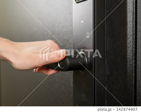A woman opens a modern smart door lock with a digital keypad and biometric fingerprint access. A woman opens a modern smart door lock with a digital keypad and biometric fingerprint access. 142874907