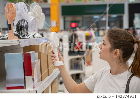 A Caucasian woman chooses a fan in a supermarket. A Caucasian woman chooses a fan in a supermarket. 142874911