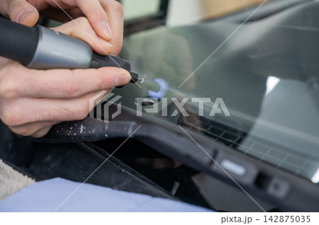 A technician drills a hole during a car windshield chip repair. A technician drills a hole during a car windshield chip repair. 142875035
