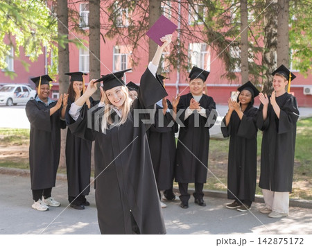 Young Caucasian woman holding diploma while classmates applaud her.  142875172