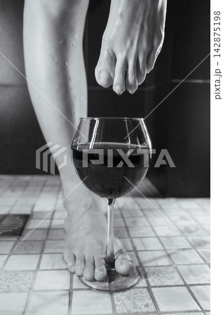 Foot fetish. A woman dips her toes in a glass of red wine. 142875198