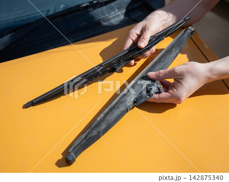 A woman replaces old windshield wipers with new ones on a car. A woman replaces old windshield wipers with new ones on a car. 142875340