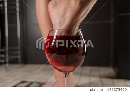 Foot fetish. A woman dips her toes in a glass of red wine. Foot fetish. A woman dips her toes in a glass of red wine. 142875420