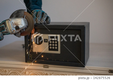 A man breaks into a safe with a grinder. A man breaks into a safe with a grinder. 142875526