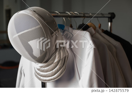 Fencing uniforms and masks hang on hangers. No people. Fencing uniforms and masks hang on hangers. No people. 142875579