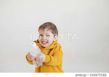A funny two-year-old boy plays with a bottle of water. A funny two-year-old boy plays with a bottle of water. 142875589