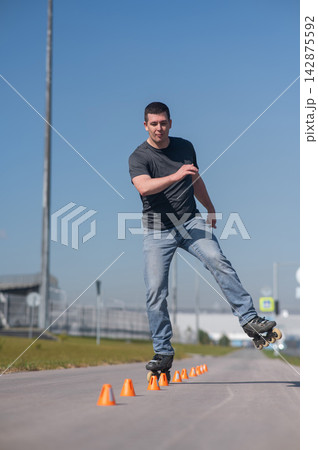 A Caucasian man rollerblades around the slalom course. 142875592