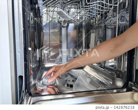 A woman's hands remove the cap from the dishwasher's salt compartment. Care for household appliances A woman's hands remove the cap from the dishwasher's salt compartment. Care for household appliances 142876218