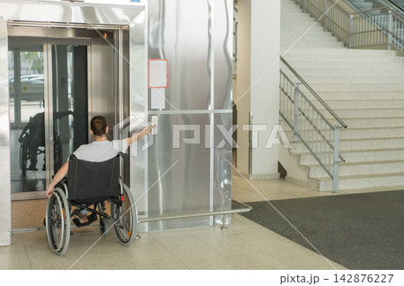 A Caucasian woman in a wheelchair uses an elevator. A Caucasian woman in a wheelchair uses an elevator. 142876227