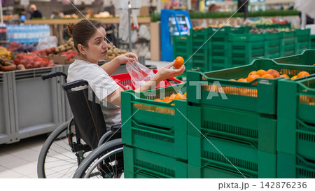 A Caucasian woman in a wheelchair buys fruit at a supermarket. A Caucasian woman in a wheelchair buys fruit at a supermarket. 142876236