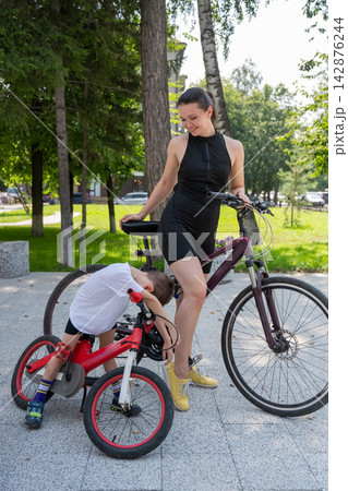 A Caucasian woman is riding a bicycle with her son. The boy fell, and the mother feels sorry for him. A Caucasian woman is riding a bicycle with her son. The boy fell, and the mother feels sorry for him. 142876244