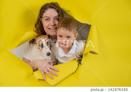 Caucasian little boy, his mother and Jack Russell Terrier dog tearing yellow paper background. Caucasian little boy, his mother and Jack Russell Terrier dog tearing yellow paper background. 142876288