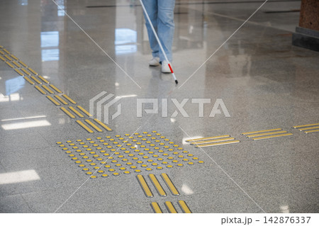 A blind woman walks on tactile paving. Close-up of her feet and a walking stick. 142876337