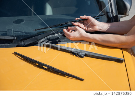 A woman replaces old windshield wipers with new ones on a car. 142876380