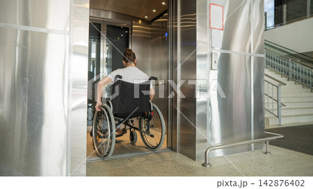 A Caucasian woman in a wheelchair uses an elevator. 142876402