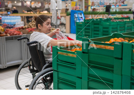 A Caucasian woman in a wheelchair buys fruit at a supermarket. A Caucasian woman in a wheelchair buys fruit at a supermarket. 142876408