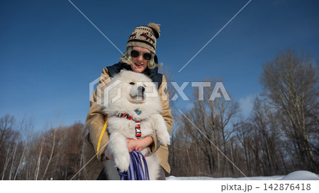 Smiling woman holding fluffy samoyed dog in snowy winter park.  142876418
