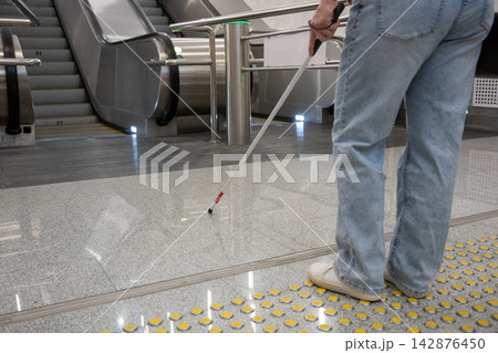 A blind woman in the metro near an escalator follows tactile navigation tiles. 142876450