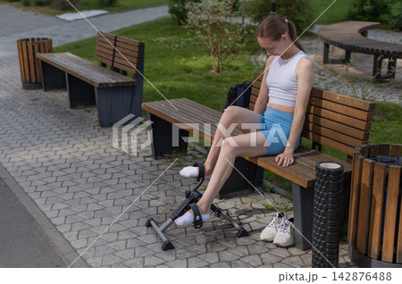 A woman uses Pedal Exercise Machine for self-rehabilitation outdoors. 142876488