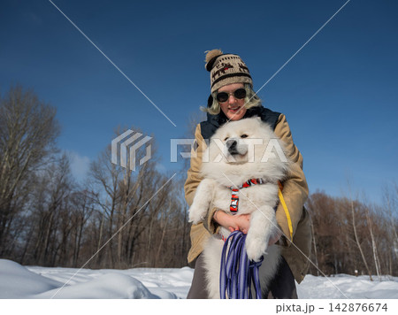 Smiling woman holding fluffy samoyed dog in snowy winter park. Smiling woman holding fluffy samoyed dog in snowy winter park. 142876674