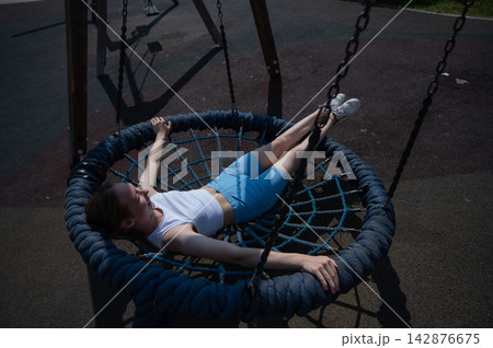 A Caucasian woman lies on a nest swing at a playground. A Caucasian woman lies on a nest swing at a playground. 142876675