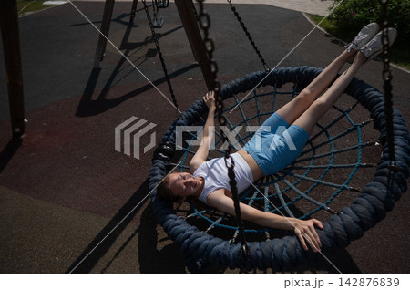 A Caucasian woman lies on a nest swing at a playground. A Caucasian woman lies on a nest swing at a playground. 142876839