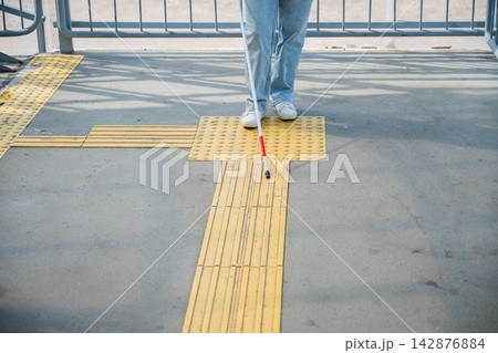 A blind woman walks using a cane and tactile tiles. A blind woman walks using a cane and tactile tiles. 142876884
