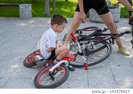 A Caucasian woman is riding a bicycle with her son. The boy fell, and the mother feels sorry for him. 142876927