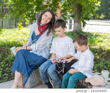 A woman and her two sons are walking a cat. 142876947