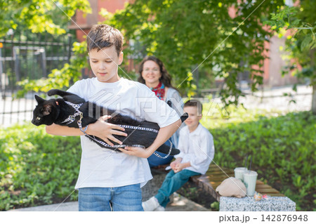 A woman and her two sons are walking a cat. 142876948