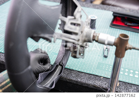 A seamstress in a workshop makes a new leather cover for a car steering wheel. A seamstress in a workshop makes a new leather cover for a car steering wheel. 142877162