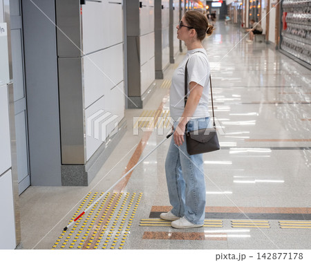 A blind woman waits for a train on the subway. A blind woman waits for a train on the subway. 142877178