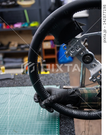 A seamstress in a workshop makes a new leather cover for a car steering wheel. A seamstress in a workshop makes a new leather cover for a car steering wheel. 142877198
