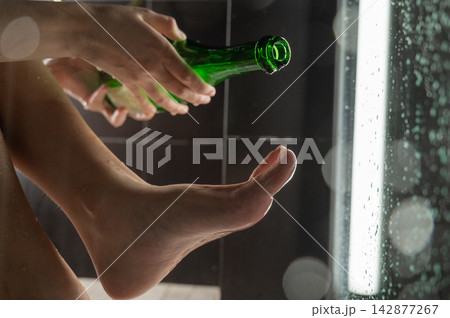 Foot fetish. A woman pours beer from a bottle onto her toes. Foot fetish. A woman pours beer from a bottle onto her toes. 142877267